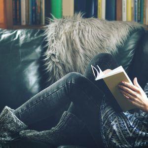 Persona leyendo un libro en un sofá de cuero con una estantería de libros en el fondo - Estrategias de marketing creativo y confiables para tu negocio que realmente funcionan - Imagen