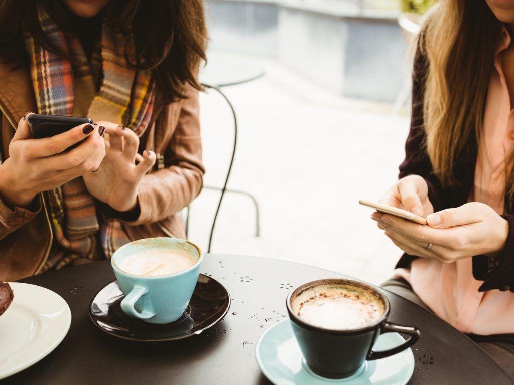 Dos mujeres enviando mensajes de texto en sus teléfonos mientras toman café - Estrategias de marketing creativo y confiable para tu negocio que realmente funcionan - Imagen